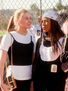 two women standing next to each other near a fence