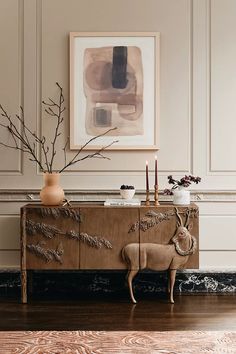 a wooden cabinet with vases and plants on it in front of a framed painting