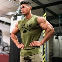 a man with his hands on his hips standing in front of a punching bag and wearing a green shirt that says do the work