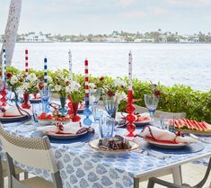 an outdoor table set with plates, glasses and watermelon flowers on the table