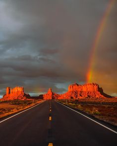 a rainbow shines in the sky over a road with mountains and clouds behind it