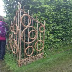 a woman standing next to a tall wooden fence made out of branches and wicker