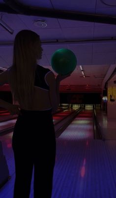 a woman holding a green frisbee in her right hand and bowling pins in the background