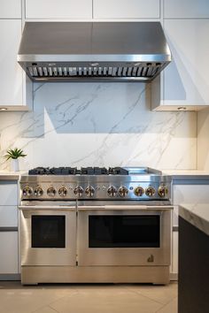 a stainless steel stove top oven in a kitchen with white cabinets and marble counter tops