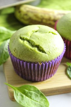 two green muffins sitting on top of a wooden cutting board next to leaves