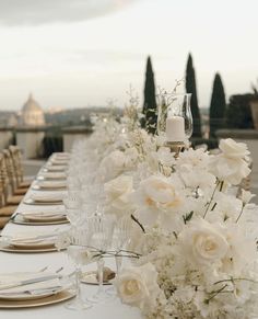 a long table is set with white flowers and place settings for an elegant dinner party