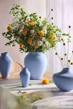 three blue vases with yellow and white flowers in them on a tablecloth covered table