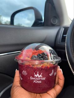 a person holding up a plastic container filled with berries and blueberries next to a car steering wheel