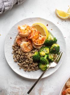 a white plate topped with shrimp, rice and broccoli next to lemon wedges