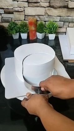 a person cutting paper with scissors on top of a black table next to potted plants