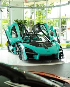 a blue sports car with its doors open in a showroom filled with windows and plants