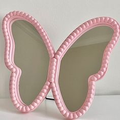 a pink butterfly shaped mirror sitting on top of a white table next to a wall