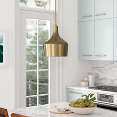 a white kitchen with marble counter tops and gold pendant light hanging over the stove top