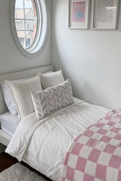 a bed with white sheets and pillows in front of a round window on the wall