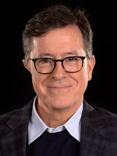 a close up of a person wearing glasses with a suit and tie on, smiling at the camera