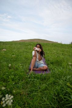 a woman sitting in the grass drinking from a bottle