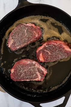 three steaks are cooking in a skillet on the stove with seasoning sprinkled over them