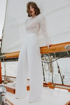 a woman standing on the deck of a sailboat wearing white pants and a lace top