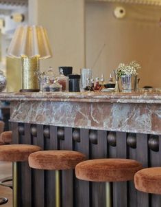 a bar with four stools in front of it and a lamp on the wall