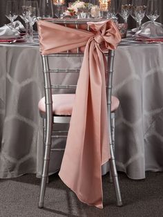 the table is set with silver chairs and pink napkins on it, along with candles