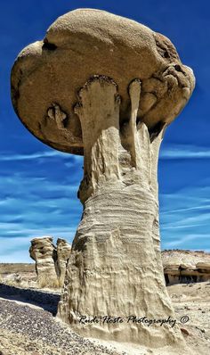 a rock formation in the desert with blue sky and clouds behind it, as seen from below