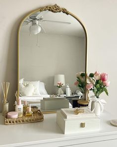 a white dresser topped with a mirror next to a vase filled with flowers and candles