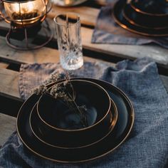 a wooden table topped with black plates and silverware