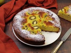 a cake with kiwi slices cut out on a plate next to a knife and fork