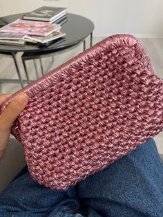 a person is sitting on the floor holding a pink purse in their hand and some magazines behind them