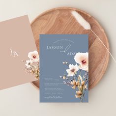 a wedding card with flowers on it next to a wooden plate and white flower bouquet