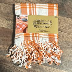 an orange and white checkered blanket on a wooden floor with a label that says robert stanley