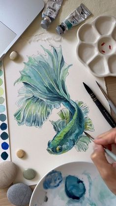 someone is painting a fish with watercolors on paper