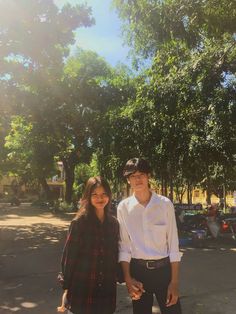 a man and woman standing next to each other in front of trees on a sunny day