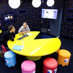 two men are sitting at a table in an office with pacman decorations on the walls