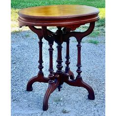 an antique wooden table with three legs and a circular top, on gravel ground in front of grass