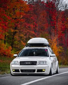 the white car is driving down the road in front of trees with red and yellow leaves