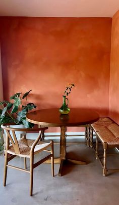 a dining room table with two chairs and a bench in front of an orange wall