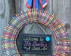 a wreath made out of crayons with a chalkboard saying welcome to mrs smith at class