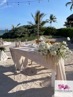 the table is set up on the beach for an outdoor wedding reception with white flowers and greenery