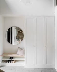 a white closet with some shoes and a round mirror