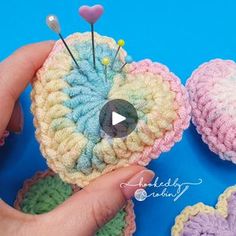 crocheted heart with pins in it being held by someone's hand on a blue background