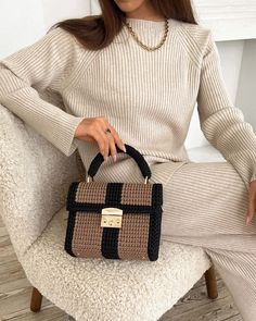 a woman sitting in a chair holding a brown and black handbag on her lap