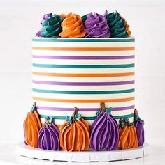 a multi - colored striped cake decorated with pumpkins and purple frosting on a white pedestal