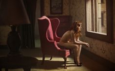 a naked woman sitting in a red chair next to a window with a lamp on it