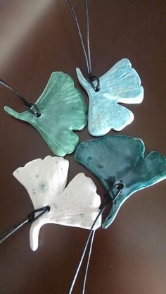 four leaf shaped glass ornaments hanging from strings on a brown table with white and green accents