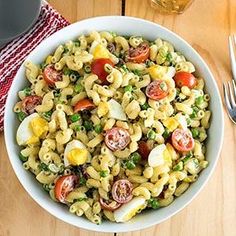 a white bowl filled with pasta salad on top of a wooden table next to silverware