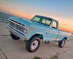 an old pickup truck parked on the side of the road near the ocean at sunset