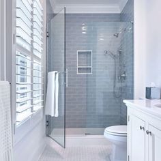 a bathroom with a walk in shower next to a white toilet and sink under a window