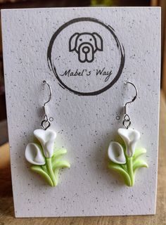 a pair of earrings with white flowers on them sitting on top of a card that reads made in may