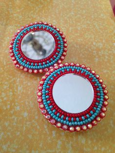 two mirrors with beaded designs on them are sitting on a yellow tablecloth and there is a small mirror in the middle